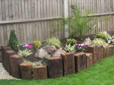 a garden with rocks and flowers in the grass next to a wooden fenced area