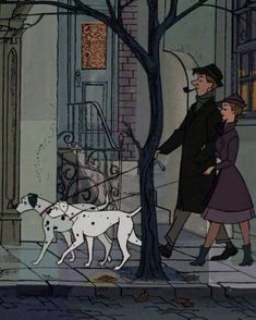 a man and woman walking two dogs down the street in front of a tree with no leaves on it