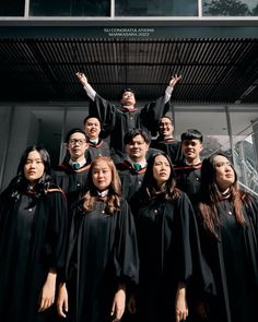 a group of people standing next to each other in front of a building with their hands up