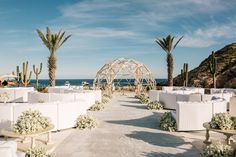 an outdoor wedding set up with white linens and flowers on the ground, surrounded by palm trees