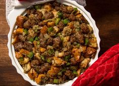 a white bowl filled with stuffing on top of a wooden table next to a red napkin