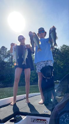 two women standing on the back of a boat holding up small fish in their hands