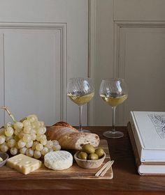 two glasses of wine, cheese and bread on a wooden table next to an open book