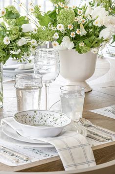 the table is set with white dishes and flowers in vases on top of it