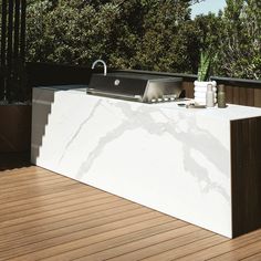 an outdoor kitchen on a wooden deck with grill and water fountain in the center, surrounded by greenery