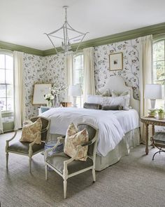 a bedroom with floral wallpaper and white bedding, two chairs in front of the bed