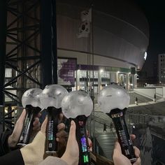 several people holding up their cell phones in front of an arena at night with lights on them