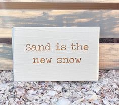 a sign that says sand is the new snow on top of some seashells