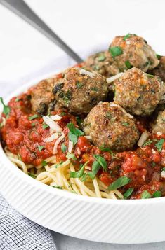 a white bowl filled with spaghetti and meatballs covered in marinara sauce, garnished with parsley