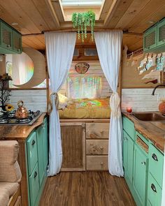 the interior of a small camper with wood flooring and green cabinetry, including curtains