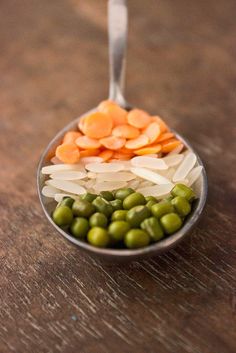 peas and carrots in a spoon on a wooden table