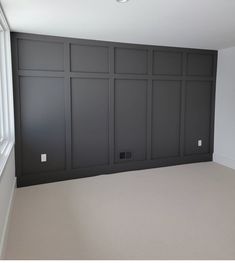 an empty room with black paneling and white trim on the walls, in front of a window