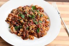 a white plate topped with pasta covered in sauce and parsley next to a fork