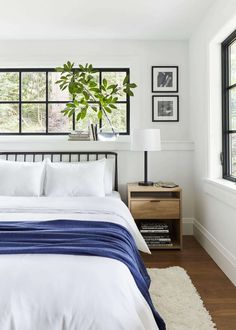 a bed with white sheets and blue blankets in a bedroom next to a large window