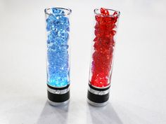 two glass vases with red and blue rocks in them sitting on a table next to each other