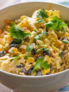 a white bowl filled with pasta salad on top of a colorful table cloth next to a wooden spoon