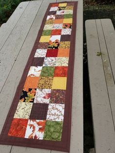 a patchwork table runner is sitting on top of a picnic table with two benches in the background