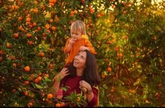 a woman holding a small child in her arms while standing next to an orange tree