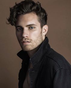 a close up of a person wearing a black shirt and jacket with his hair pulled back