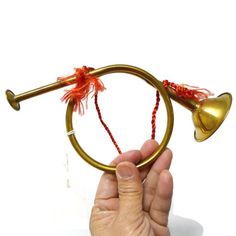 a hand holding a brass colored instrument with red string and bells on it's end