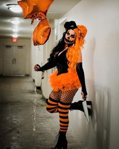 a woman dressed up as a clown with orange hair and black stockings, holding balloons