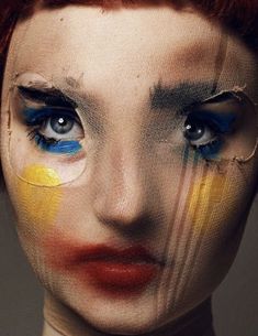 a woman with red hair and blue eyes has painted her face orange, yellow and blue