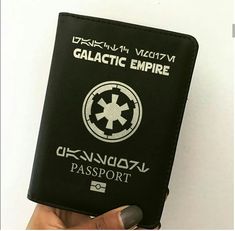 a person holding up a black passport with the galactic empire logo in white on it