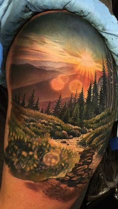 a man's arm with a painting on it that has trees and mountains in the background