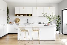 two bar stools sit in front of an island with white cabinets and wood floors