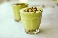 two glasses filled with green smoothie on top of a white tablecloth covered table