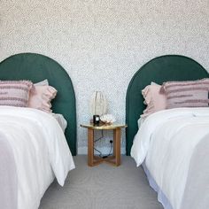 two twin beds with white and pink bedding in front of a wallpapered background