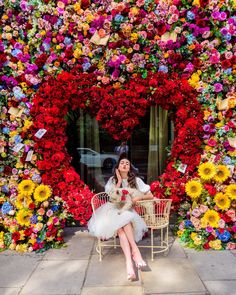 a woman sitting on a chair in front of a flower wall with flowers all over it