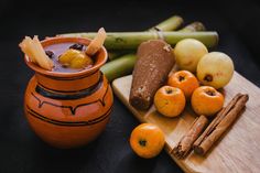 a wooden cutting board topped with oranges and other fruits next to a vase filled with fruit