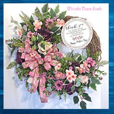 a wreath with pink flowers and greenery on it is displayed in front of a blue frame