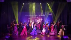 a group of women dancing on stage with their arms in the air and lights behind them