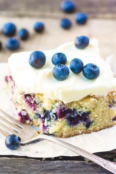 a piece of cake with white frosting and blueberries on top next to a fork