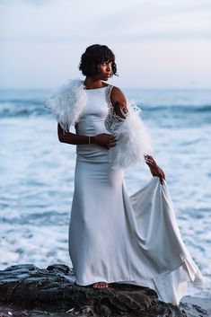 a woman in a white dress standing on rocks near the ocean