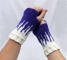 two hands wearing purple and white knitted wrist warmers, one holding the other