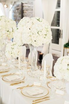 the table is set with white flowers and gold place settings for an elegant wedding reception