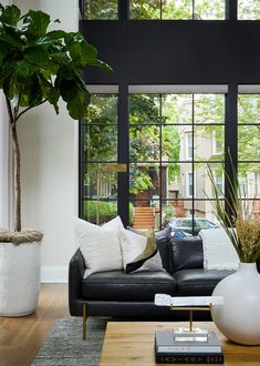 a living room with black leather couches and large windows in the back ground area