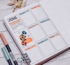 an open planner book sitting on top of a wooden table next to a pen and flower