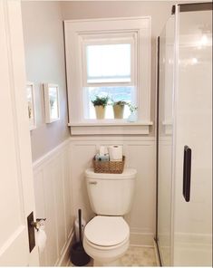 a white toilet sitting in a bathroom next to a shower and sink with two plants on the window sill