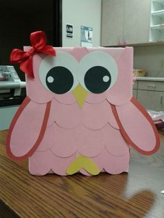 an owl shaped box sitting on top of a wooden table with a red bow around its neck