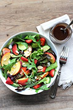 a salad with strawberries, cucumbers and almonds in a white bowl