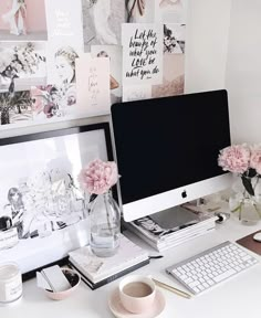 a white desk topped with a computer monitor next to a cup and vase filled with pink flowers