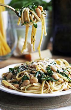 pasta with spinach and chickpeas being lifted from a white plate by a fork