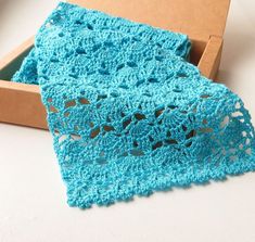 a blue crocheted scarf sitting on top of a table next to a cardboard box