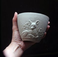 a hand holding a white ceramic cup with a deer on it