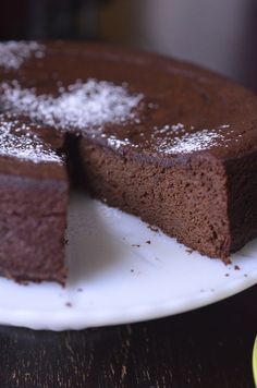 a chocolate cake with powdered sugar on top sits on a white plate next to an orange