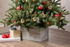 a small christmas tree with red and gold ornaments in a wooden box on the floor